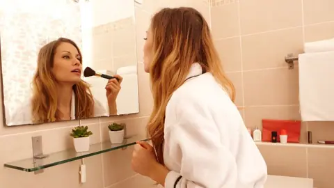 Kobieta maluje się w łazience przed lustrem